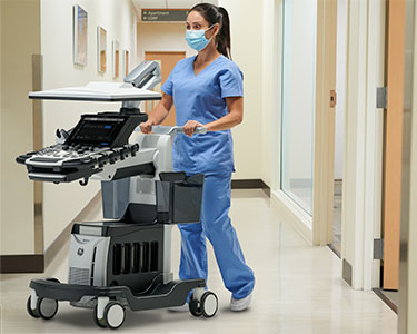 Female clinician pushing an ultrasound system down a hospital hallway