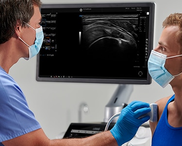 Male clinician doing a shoulder ultrasound scan on a male patient