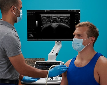 Male clinician scanning a male patient's shoulder with ultrasound
