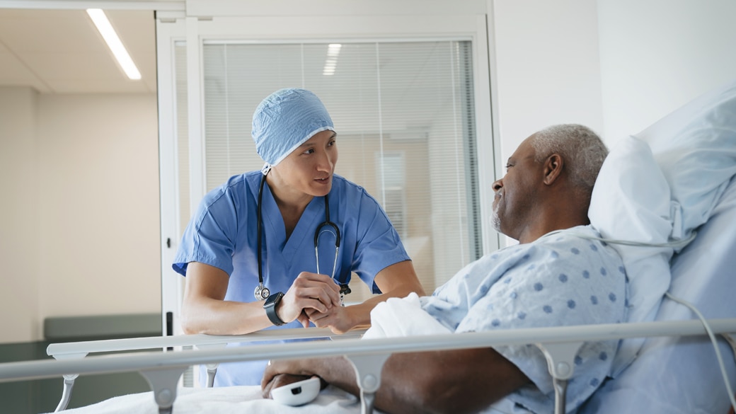 cardiologist in surgical scrubs talking to male patient at bedside