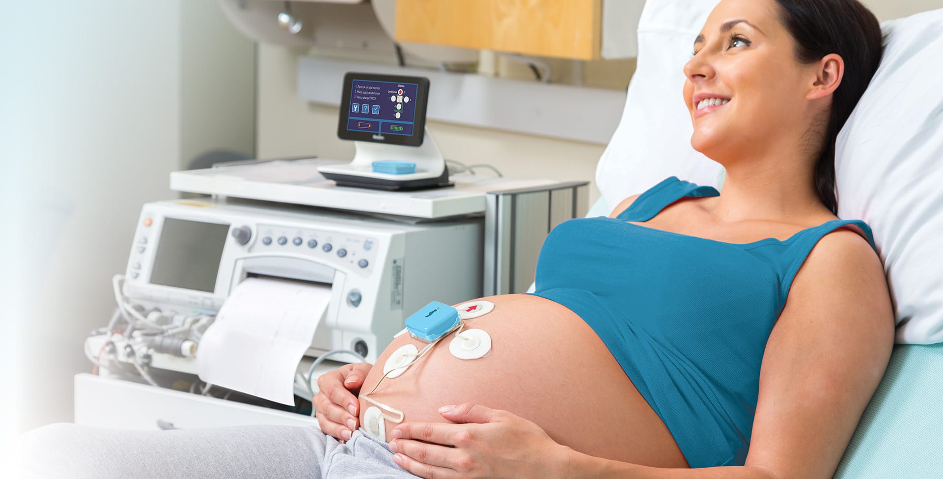 pregnant woman holding belly with monica novii attached in hospital setting
