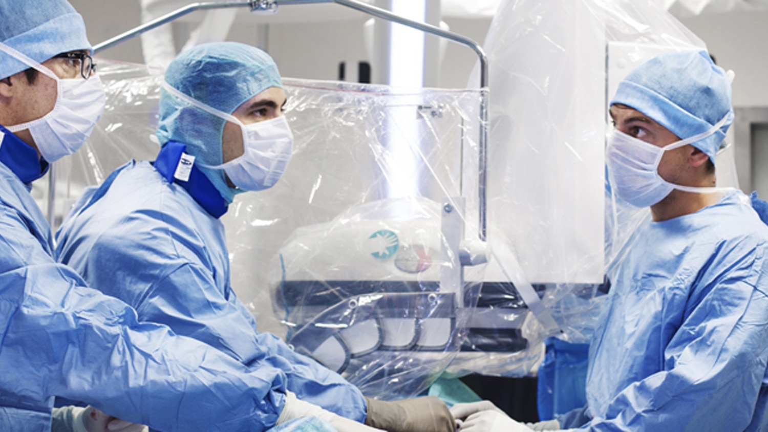 Tres doctores en batas azules usando los sistemas intervencionistas guiados por imágenes.