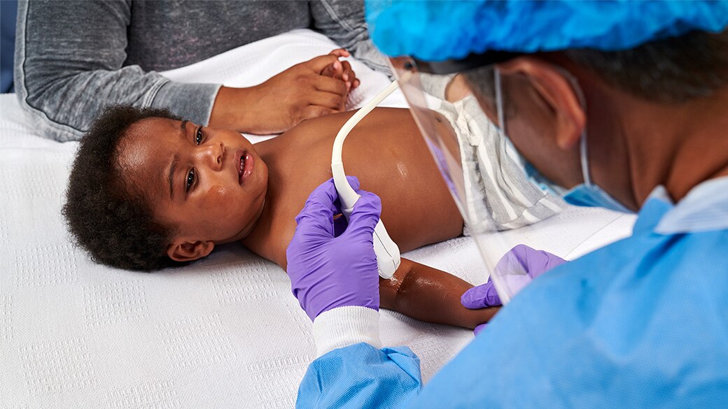 healthcare provider using a small ultrasound probe on a NICU/PICU patient